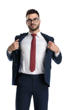 Genç iş adamı ayakta ve ceketini çıkarırken beyaz stüdyo arka planında mutluydu.