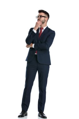 Çekici iş adamı kollarını kavuşturmuş ve beyaz stüdyo arka planında çenesine dokunmuş gözlük takıyor.