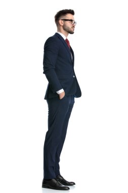 Gözlüklü seksi bir adamın yan görünüşü. Elleri cebinde ve ileriye bakıyor. Beyaz stüdyo arka planında.