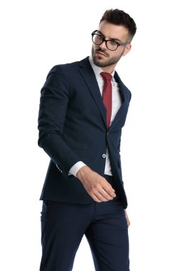Gözlüklü seksi bir adam beyaz stüdyo arka planında havalı bir tavırla arkasını kolluyor.