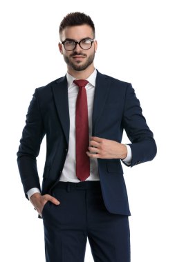 Genç iş adamı gözlük takıyor, el ele duruyor ve beyaz stüdyo arka planında mutlu bir şekilde ceketini tamir ediyor.