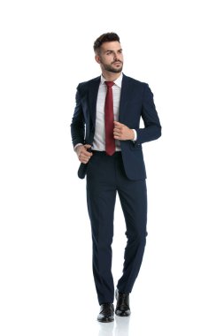 Yakışıklı iş adamı ceketini düzeltirken donanma elbisesi giyiyor ve beyaz stüdyo geçmişine bakarak başını çeviriyor.