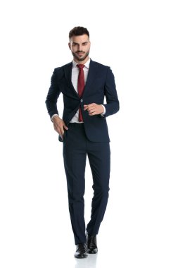 Yakışıklı işadamı elini cebinden çıkarırken yürürken beyaz stüdyo arka planında mutlu bir şekilde yürüyor.