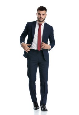 Beyaz stüdyo arka planında ceketini düzenlerken denizci kıyafeti giyen seksi iş adamı yürüyor.