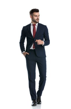 Genç resmi adam donanma takımı giyiyor, cebinde ve beyaz stüdyo arka planında mutlu bir şekilde yan yana yürüyor.