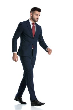 Beyaz stüdyo arka planında ciddi yürüyen, denizci kıyafeti giyen seksi bir iş adamının yan görüntüsü.