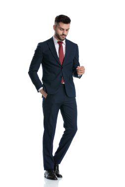 Yakışıklı iş adamı donanma takımı giyiyor, el ele yürüyor ve beyaz stüdyo arka planında stil sahibi bir şekilde aşağı bakıyor.