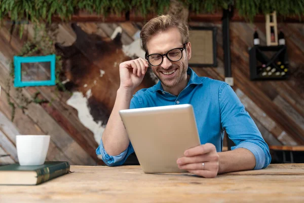 Przypadkowy Mężczyzna Okularach Siedzący Przy Biurku Patrzący Swój Tablet Szczęśliwy — Zdjęcie stockowe