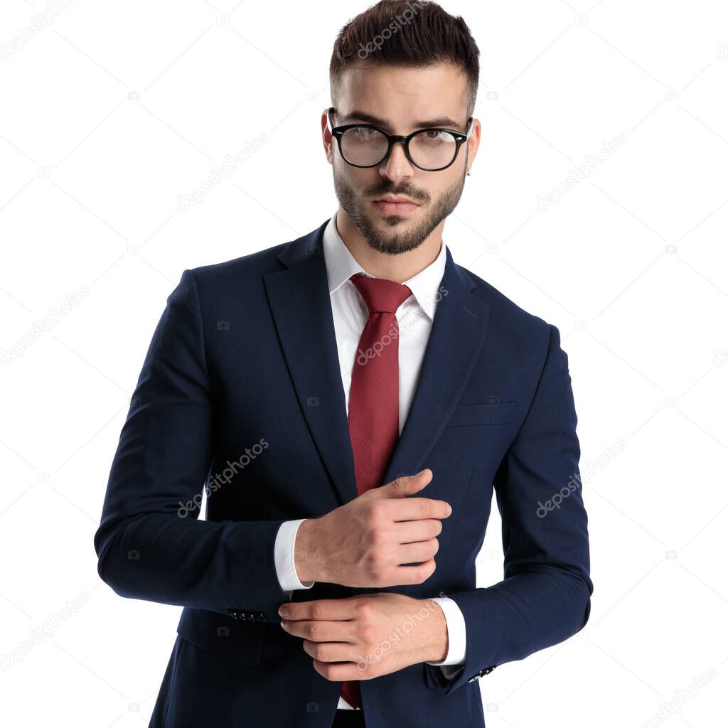 young businessman wearing glasses standing and adjusting sleeve while striking a pose with serious attitude on white studio background