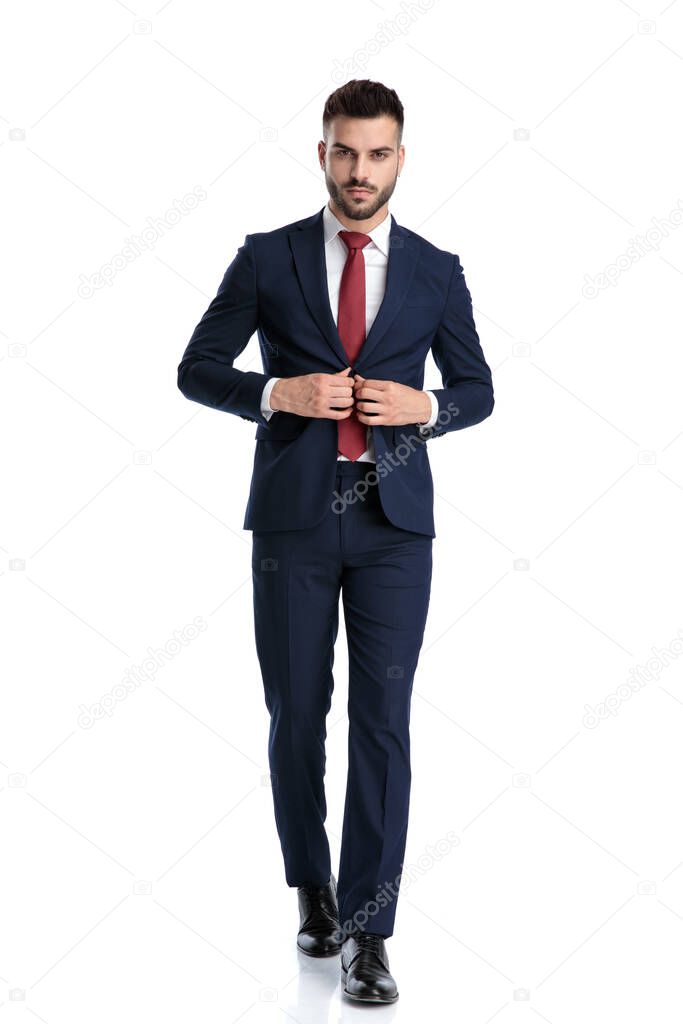 young businessman wearing navy suit walking while unbuttoning his jacket cool on white studio background