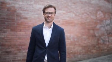 Gözlüklü akıllı sarışın iş adamı dışarıda gülümserken yürüyor ve etrafa bakıyor.