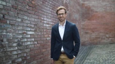 Zeki, sıradan, seksi iş adamı bir eli cebinde diğeriyle birlikte bir çanta tutuyor ve gözlük takıyor.