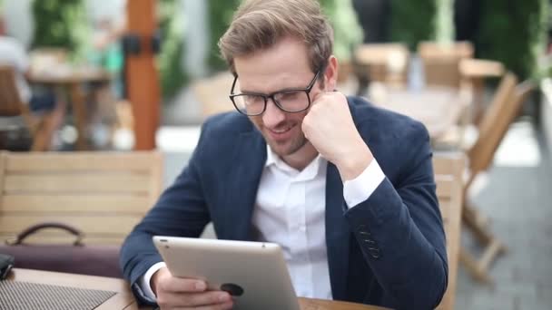 Aantrekkelijke Jonge Zakenman Met Bril Lezen Zijn Tablet Terwijl Zitten — Stockvideo