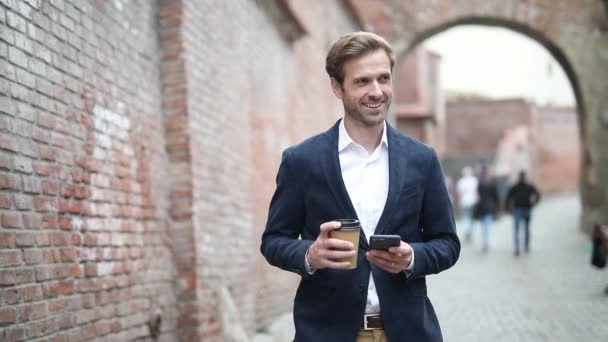sexy smart casual Geschäftsmann läuft, während er telefoniert, eine Tasse Kaffee trinkt und einen Marineanzug trägt, im Freien