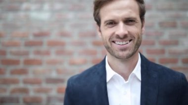 Genç, sarışın bir iş adamının, donanma kıyafeti giyip, yüzünde kocaman bir gülümsemeyle kameraya bakarken duvarın karşısında durmasını.