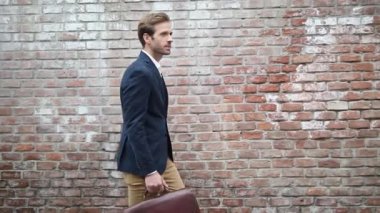 Genç ve çekici bir işadamının, donanma kıyafeti giyip, elinde bir evrak çantası tutarken, yürürken ve etrafına bakınırken yan görüntüsü.