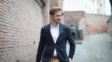 Denizci kıyafeti giyen akıllı sıradan bir işadamı bir eli cebinde yürürken tuğla duvarın yanına bakıyor.