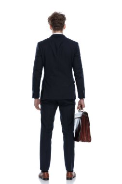 Takım elbiseli ve beyaz stüdyo arka planında duran bir iş adamının evrak çantasını tutuşu.