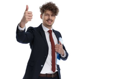 Pozitif iş adamı elinde bir pano tutuyor. Takım elbise giyerken gülümsüyor ve beyaz stüdyo arka planında duruyor.