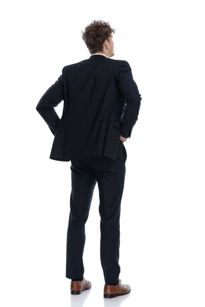 リアビュー希望のビジネスマンは スーツを着ている間 彼の腰に手を保持し 白いスタジオの背景に立って — ストック写真