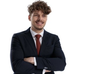 Mutlu iş adamı elleri çaprazlı gülerken takım elbise giyer ve beyaz stüdyo arka planında durur.