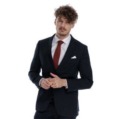 Kararlı iş adamı takım elbise giyerken ve beyaz stüdyo arka planında dururken elleriyle oynuyor.