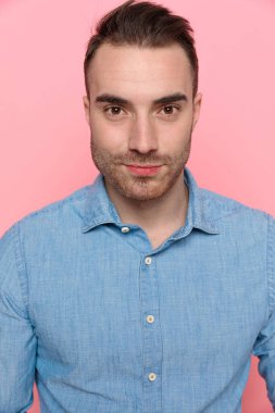 Mavi tişörtlü yakışıklı bir adamın portresi. Pembe stüdyo arka planında dikilip kameraya bakıyor.