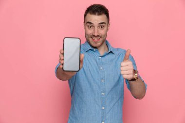 Çekici, heyecanlı, sıradan bir adam. Telefonunu gösteriyor ve pembe stüdyo arka planında 