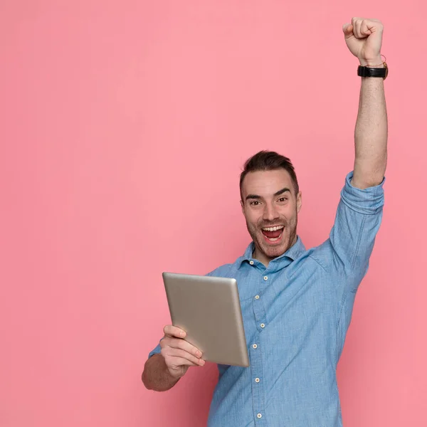 英俊而随意的男人庆祝成功 拿着平板电脑 在粉红的工作室背景下开怀大笑 — 图库照片