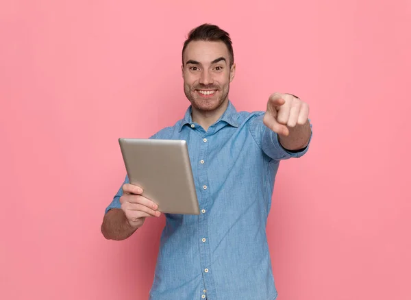 若いカジュアルな男が前を向いてタブレットにメッセージを書きピンクのスタジオの背景に笑顔で — ストック写真