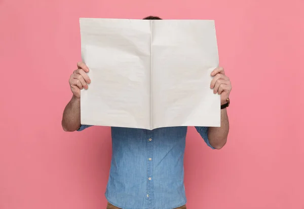 カジュアルな男がピンクのスタジオで新聞の後ろに顔を隠して — ストック写真