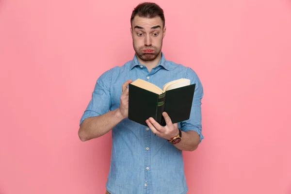 Bello Sorpreso Uomo Casuale Guardando Attraverso Libro Soffiando Guance Sfondo — Foto Stock