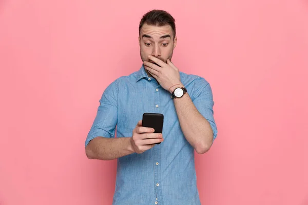 Удивлен Случайный Мужчина Трогает Лицо Глядя Телефон Розовом Фоне Студии — стоковое фото