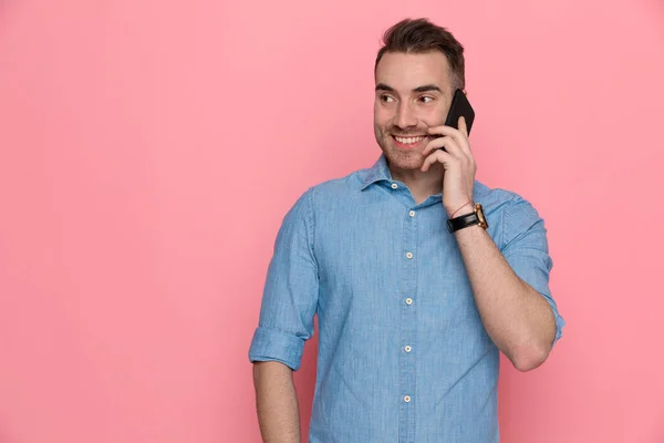 電話で話してるハンサムな若いカジュアルな男はピンクのスタジオの背景を見て笑ってる — ストック写真