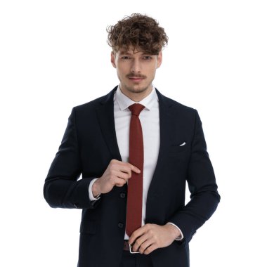 Yakışıklı iş adamı takım elbise giyerken kravatını düzeltiyor ve beyaz stüdyo arka planında duruyor.