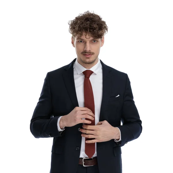 スーツを着て白いスタジオの背景に立っている間 彼のネクタイを固定するビジネスマンを自信を持って — ストック写真