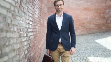 Çekici sarışın iş adamı bir elinde evrak çantası, gözlük takıyor, gülümsüyor ve baş parmağını kaldırıyor.