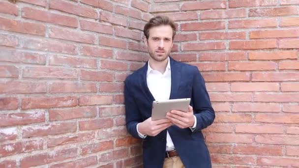 Knappe Blonde Zakenman Leunend Een Stenen Muur Sms Zijn Tablet — Stockvideo