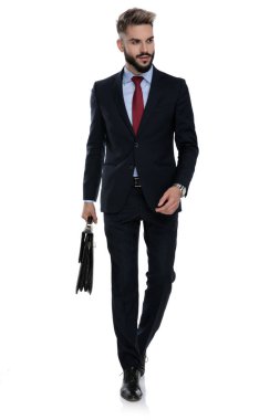 Mutlu genç işadamı beyaz arka planda tek başına yürür ve bavulu tutar.