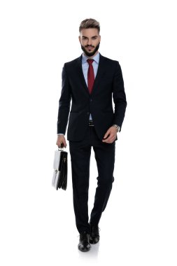 Gülümseyen genç işadamı bavulu tutuyor ve beyaz arka planda tek başına yürüyor.