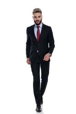 Beyaz arka planda yalnız yürüyen takım elbiseli seksi genç iş adamı.