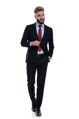 Kendine güvenen genç işadamı ceketini ayarlıyor ve beyaz arka planda tek başına yürüyor.