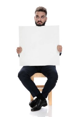 Takım elbiseli genç işadamı boş tahtayı sunuyor ve beyaz arka planda tek başına oturuyor.