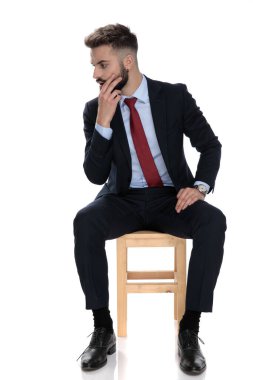 Şok olmuş genç işadamı beyaz arka planda tek başına oturuyor ve el ele tutuşuyor.