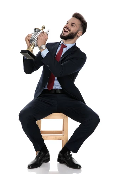Orgulhoso Jovem Empresário Terno Sorrindo Apresentando Troféu Para Lado Sentado — Fotografia de Stock