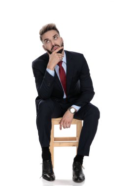 Düşünceli genç işadamı el ele tutuşup düşünüyor, beyaz arka planda tek başına oturuyor.