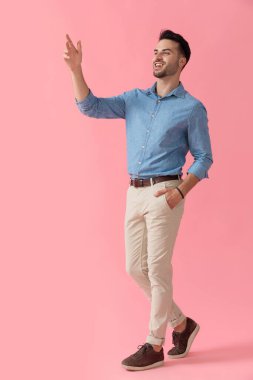 Çekici iş adamı mavi gömlekli, el ele yürüyor ve pembe stüdyo arka planında selam veriyor.