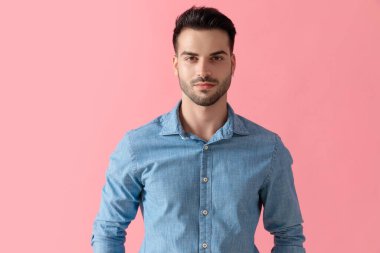 Çekici iş adamı mavi gömlek giyiyor ve pembe stüdyo arka planında mutlu bir şekilde kameraya bakıyor.