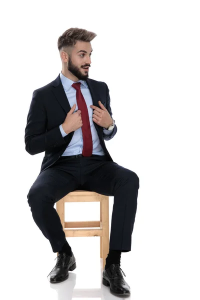 stock image happy young businessman smiling and poiting finger to himself, sitting isolated on white background