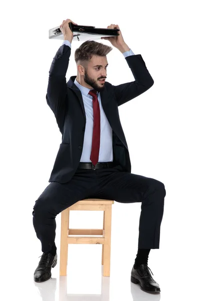 Jovem Empresário Terno Segurando Mala Acima Cabeça Lutando Sentado Isolado — Fotografia de Stock